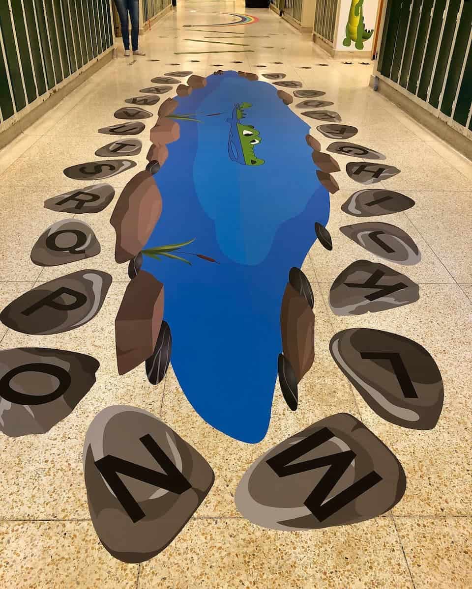 Colorful sensory path with a crocodile design and alphabet stones in a hallway.